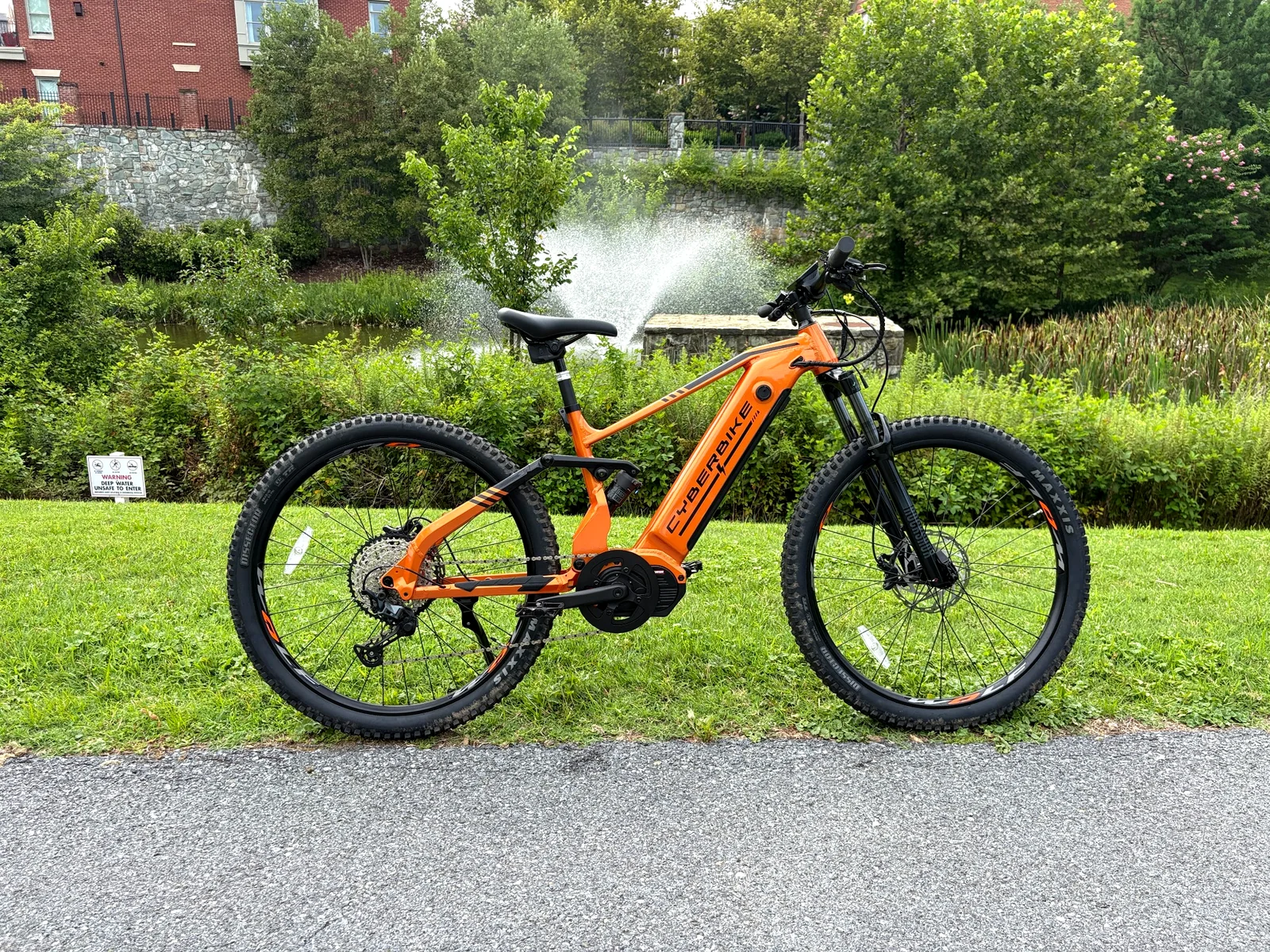 Orange 2026 Cyberbike Raptor full-suspension electric mountain bike beside a landscaped pond