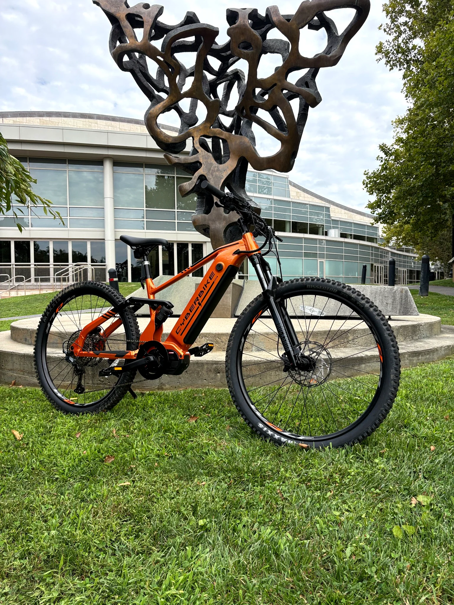 Orange Cyberbike Raptor eMTB photographed outdoors in an urban park setting
